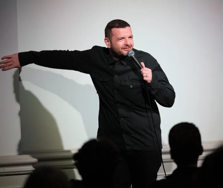 A comedian on stage in front of the Soho Comedy Factory sign