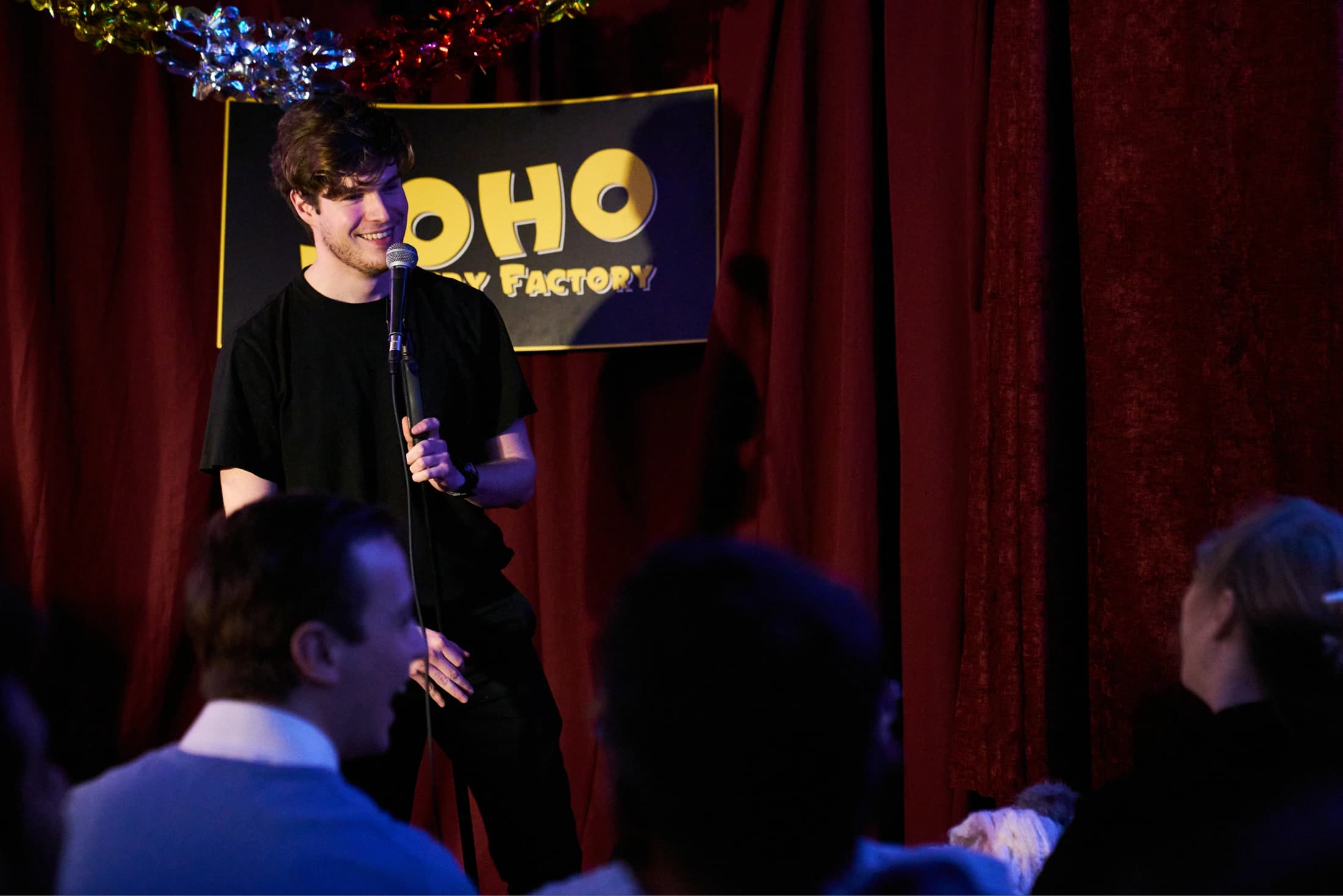 A comedian on stage in front of the Soho Comedy Factory sign